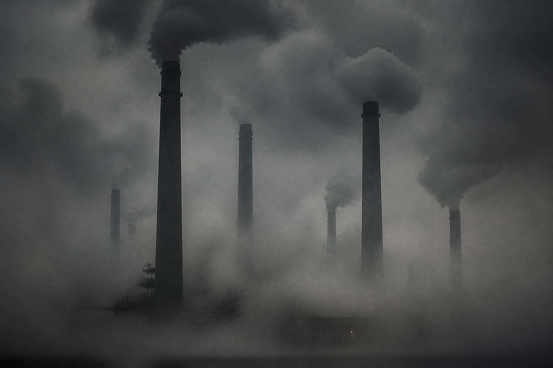 Industrial smokestacks rising through heavy fog at dusk